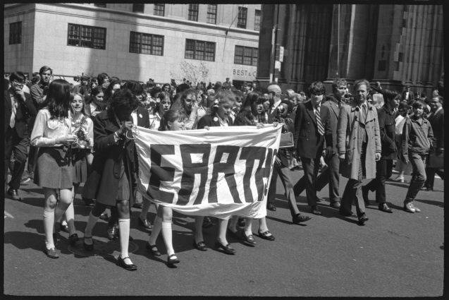 Black and white image - 1970s demonstrators walk with a sign that says EARTH
