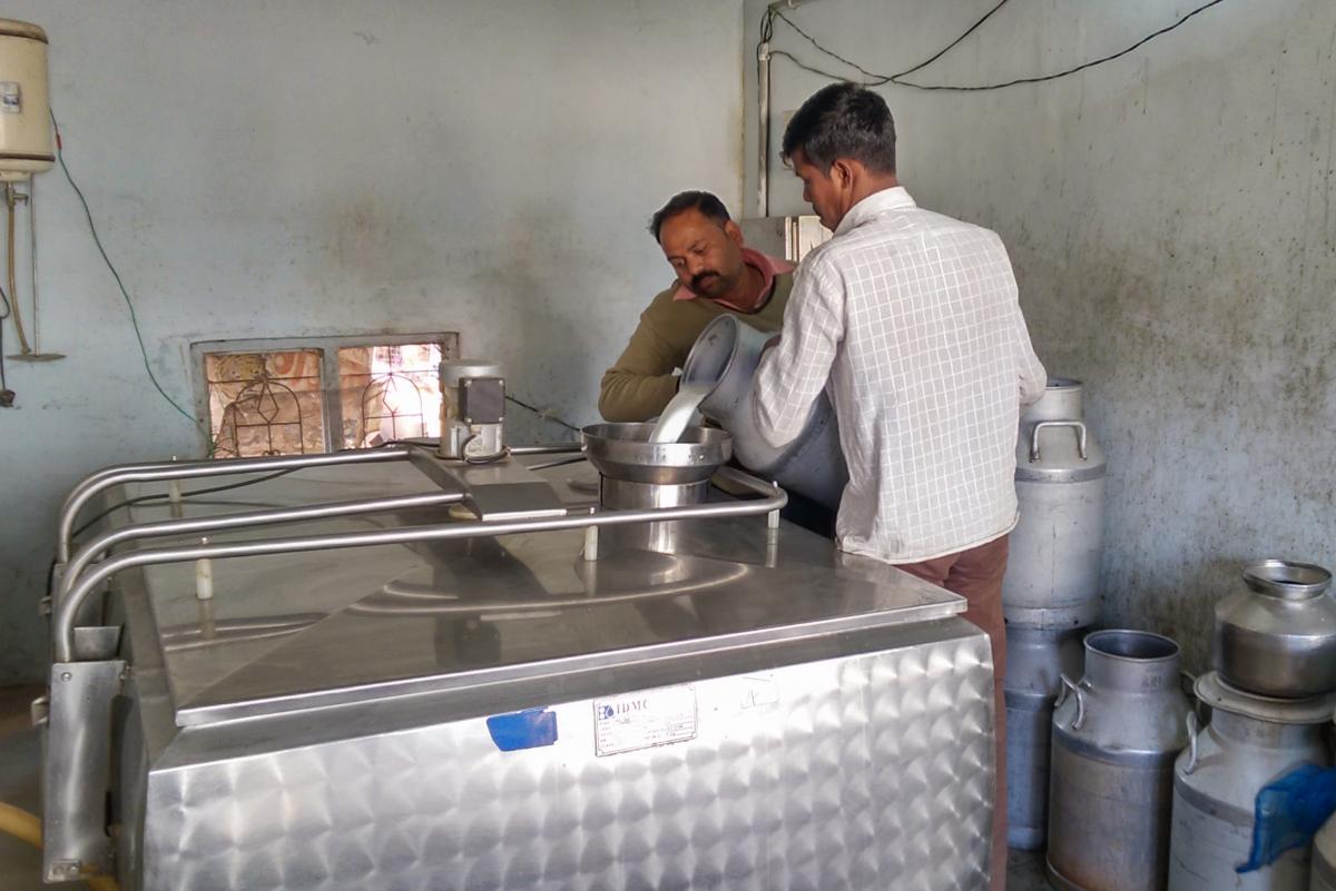 Two men pour large container of milk into machine
