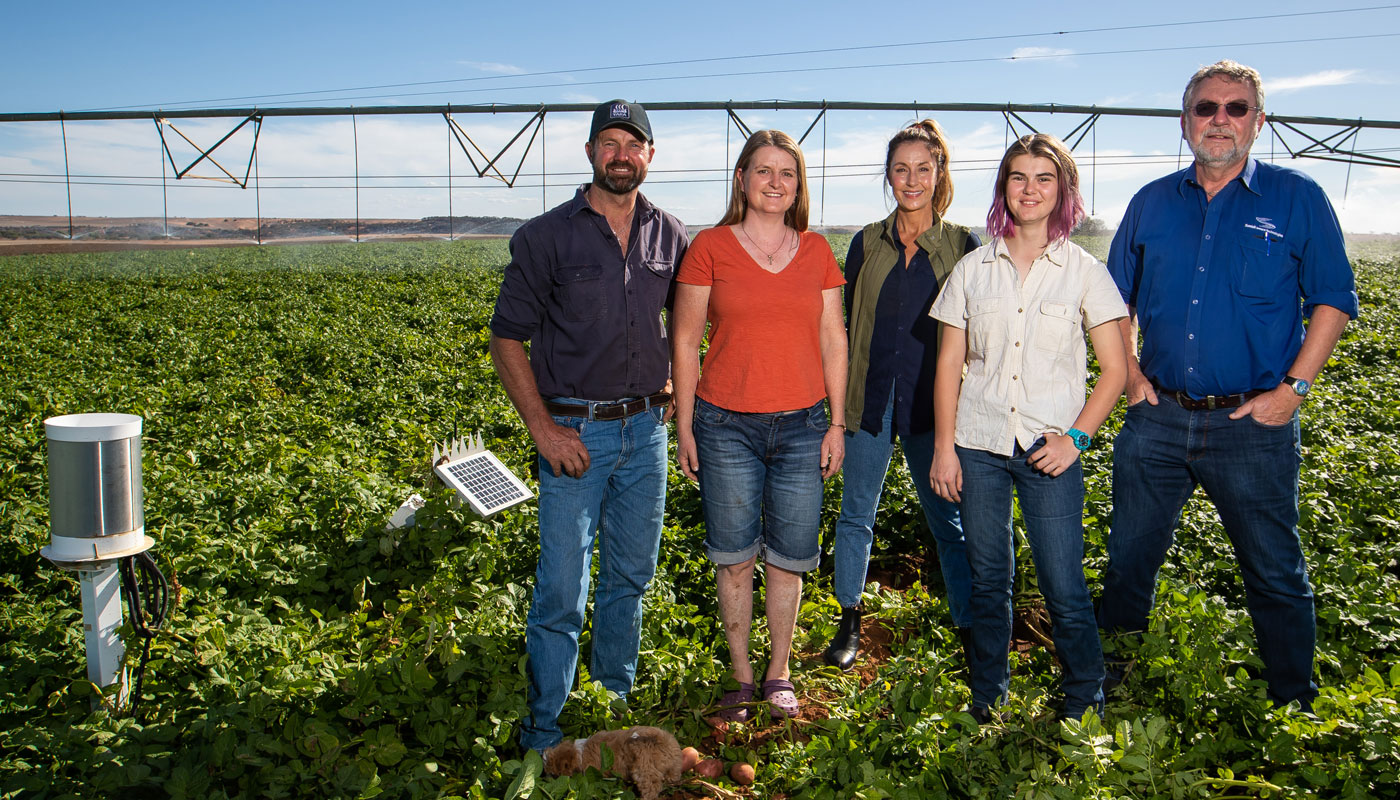 Five adults standing in potato field sprayer in back sensors in the field
