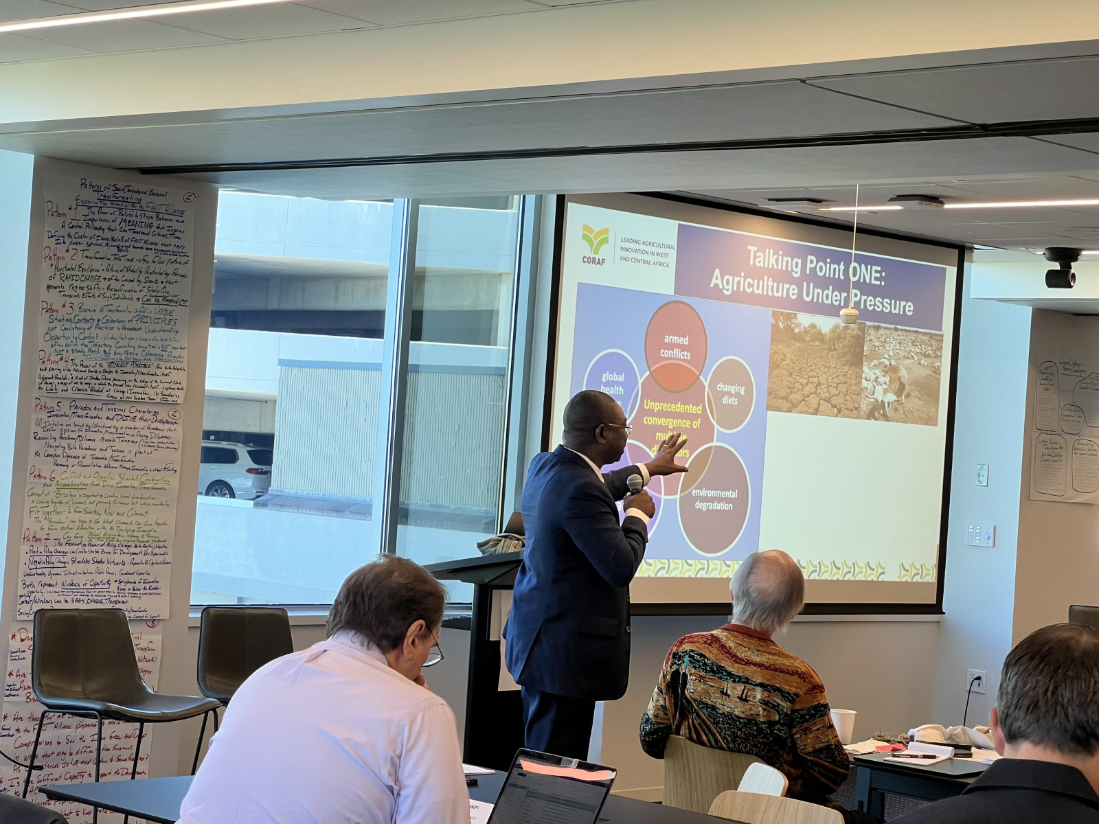 Abdou Tenkouano giving a presentation pointing to slides on a large projection screen