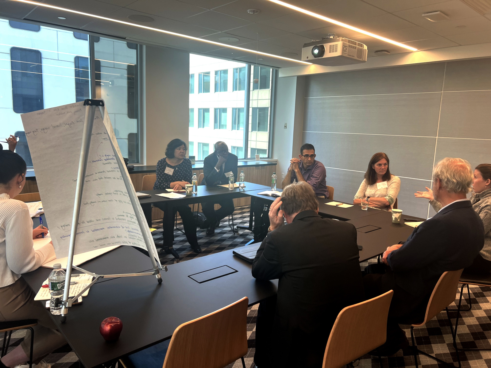 People sitting around a U-shaped conference room table with a flip chart on an easel