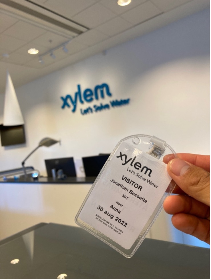 A hand holding up a Xylem visitor's pass in a plastic lanyard, with the Xylem logo on a white wall in foreground