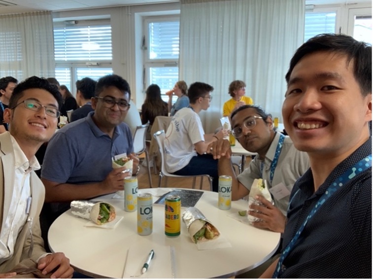 Four men smiling at the camera during a lunch around a circular table