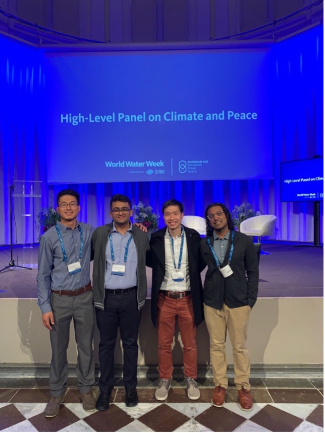Four men standing arm and arm in front of a blue projector screen that says World Water Week