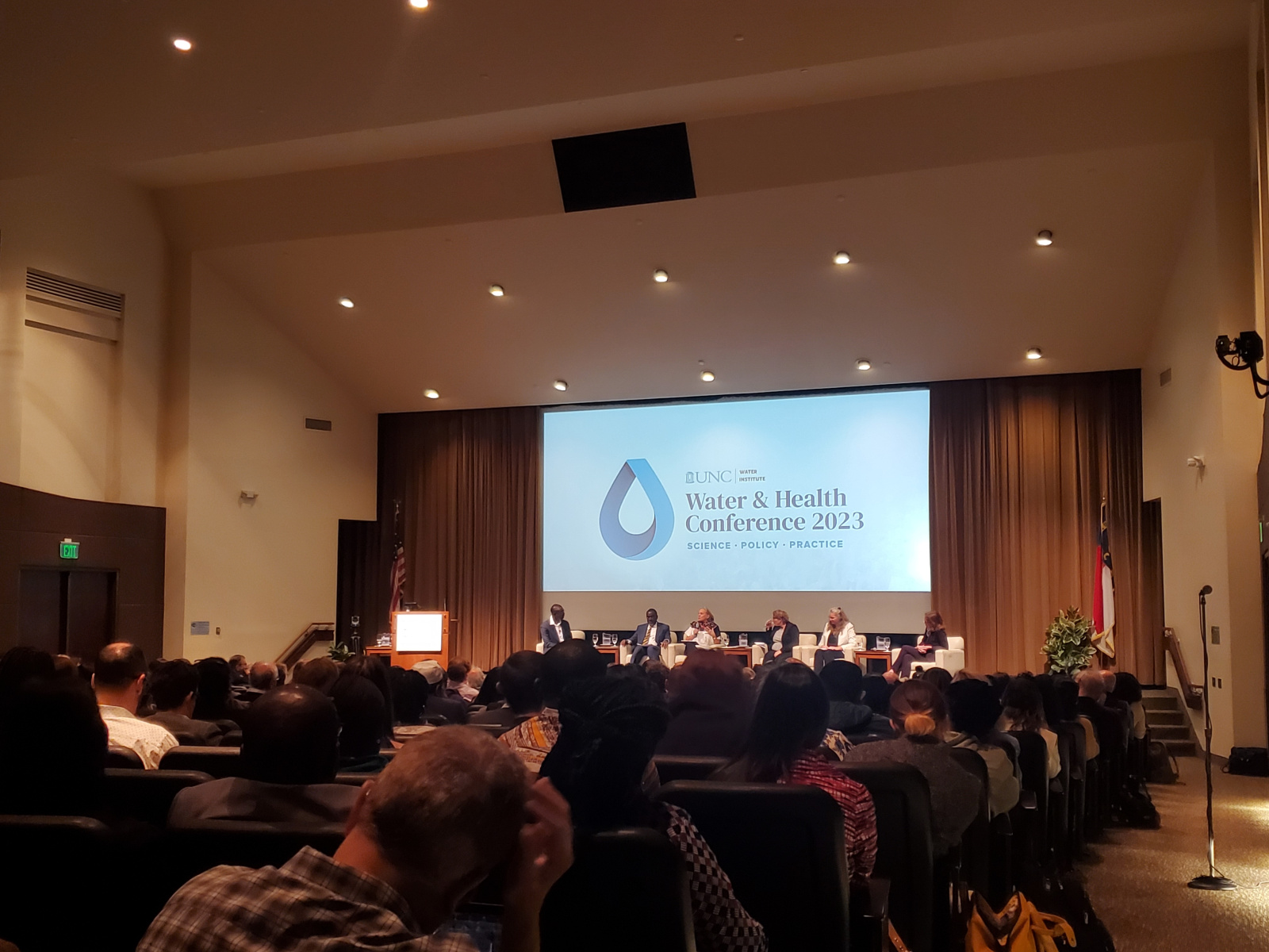 Six people sitting on a stage below a projector screen displaying the UNC Water & Health Conference logo.
