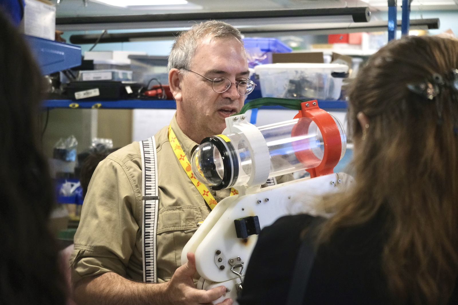 Andrew Bennett holds a MIT Sea Grant's prototype in a lab setting, with two viewers in the foreground