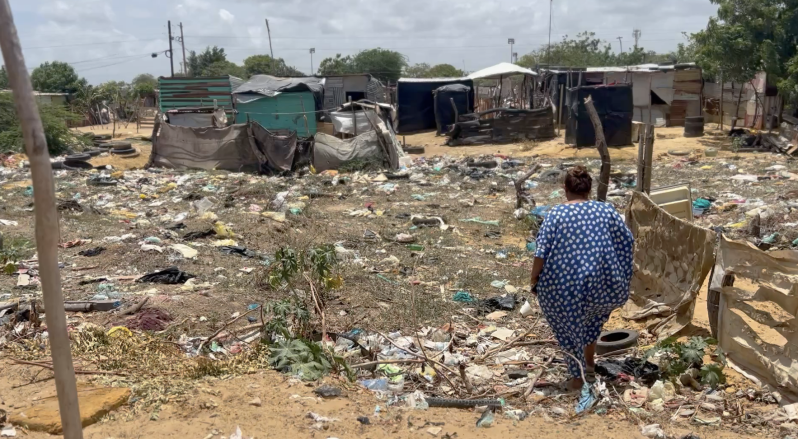 A woman gazing out to various makeshift homes made of metal scraps and sheets. The ground is covered to liter