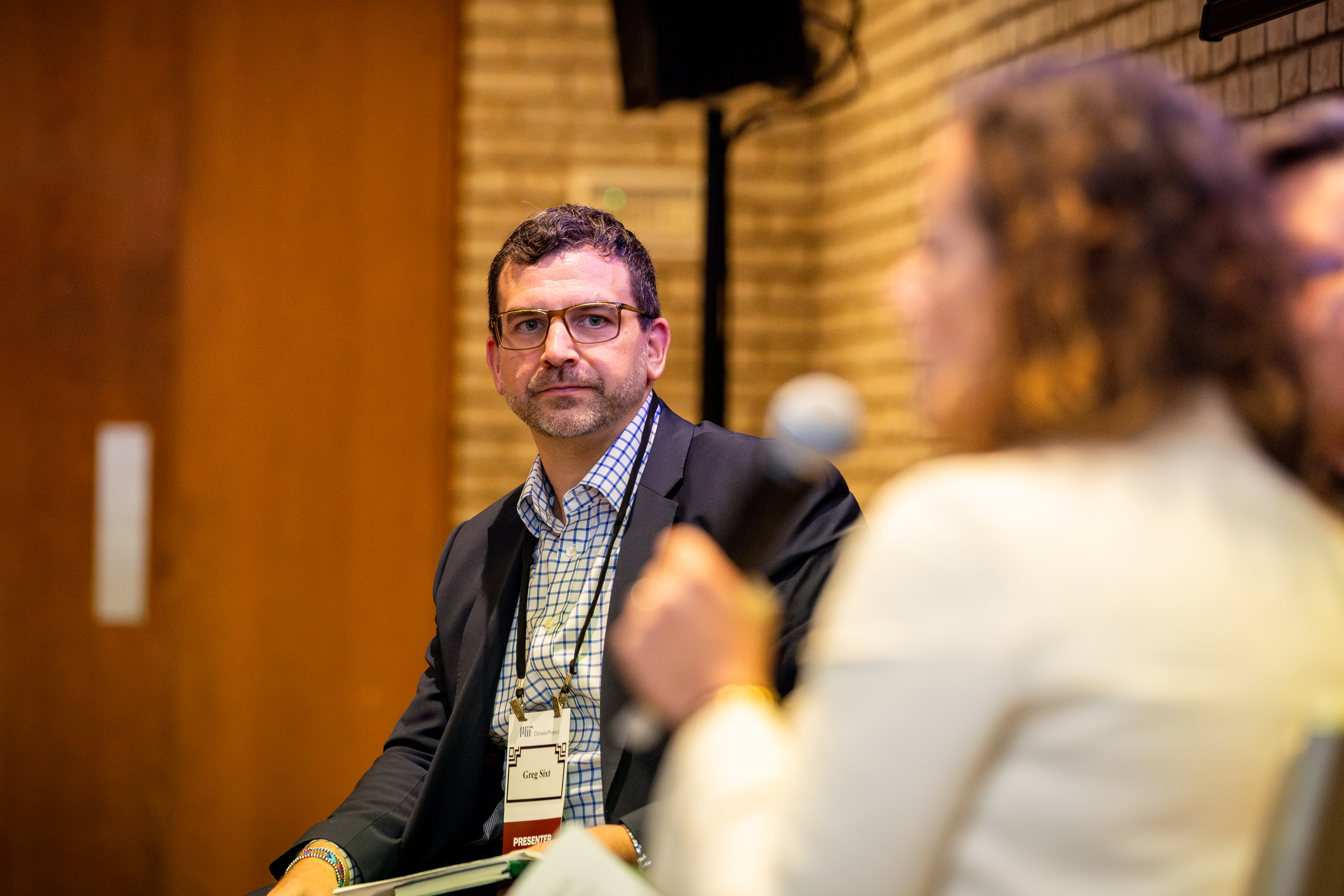 Greg Sixt moderates the panel and looks on as Paola de Almeida speaks into a microphone