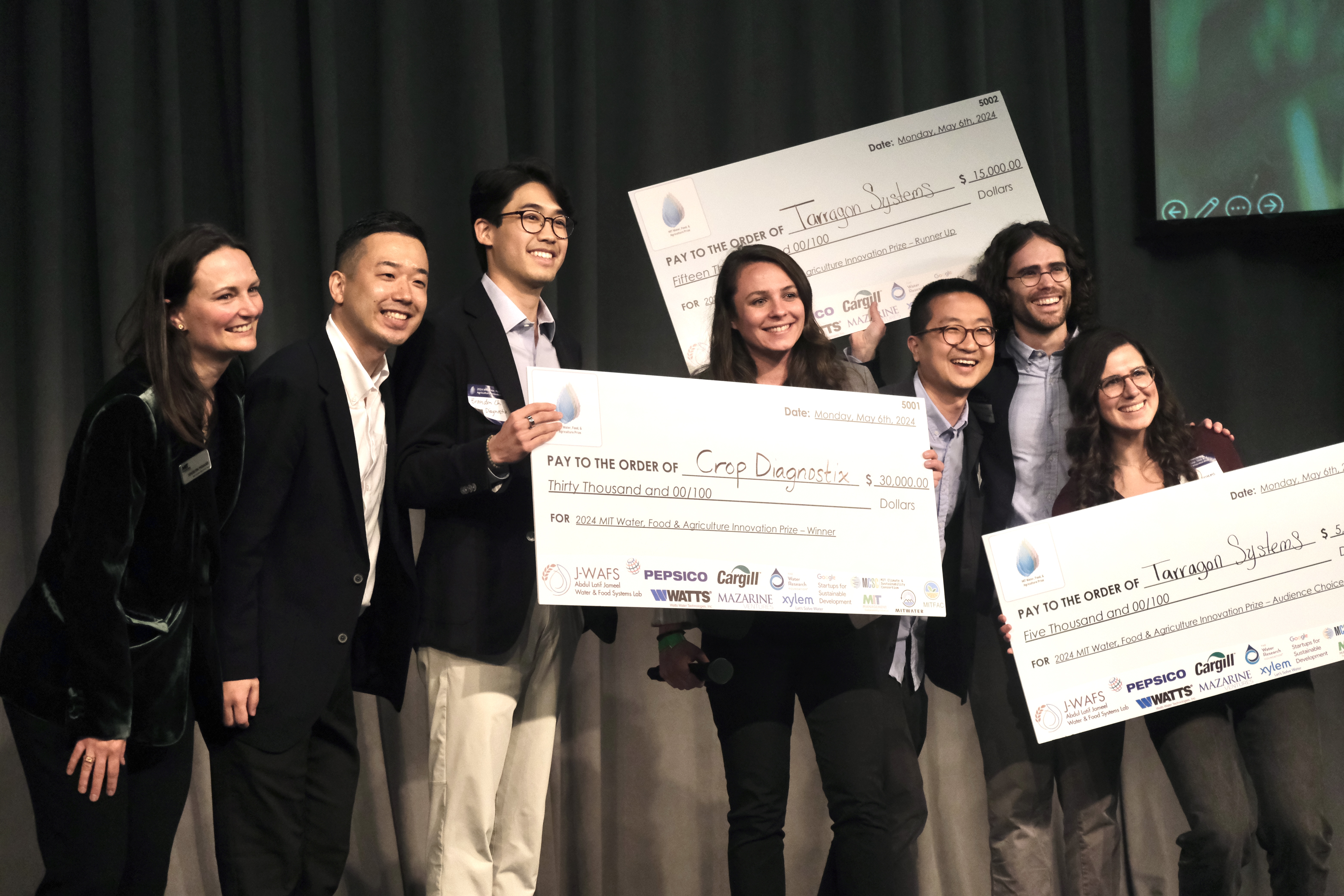 Award winners stand on a stage in an auditorium holding large checks