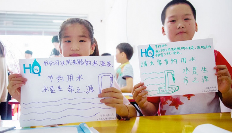 Two children hold pictures they drew with the MyH2O logo