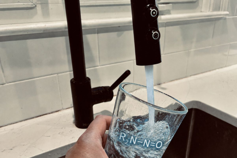 A hand holding a glass that is being filled with water from a kitchen sink tap