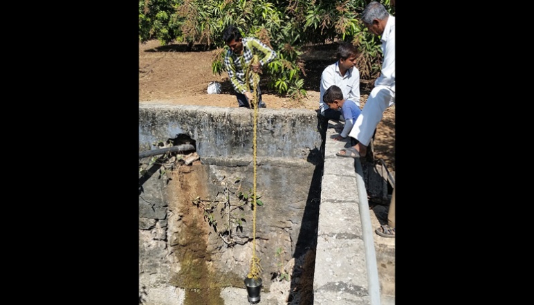 Researcher lowering bucket into well to measure groundwater quality