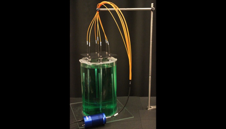 Cycindrical tank containing green fluid and glass rods connected to wires. 
