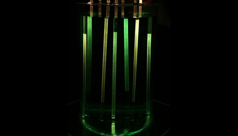 Glass rods glowing in cylindrical tank filled with green fluid. 