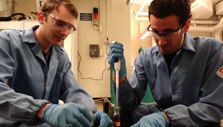 Two researchers pipetting from vials at lab bench
