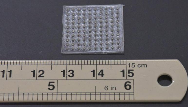 Microneedle array of 10 x 10 needles next to a ruler