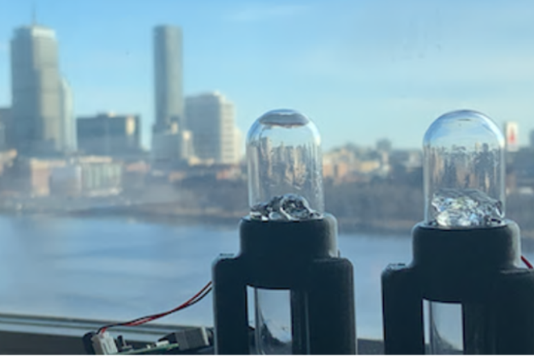 Two sensor devices in front of a window overlooking a city skyline, used for scientific measurements.