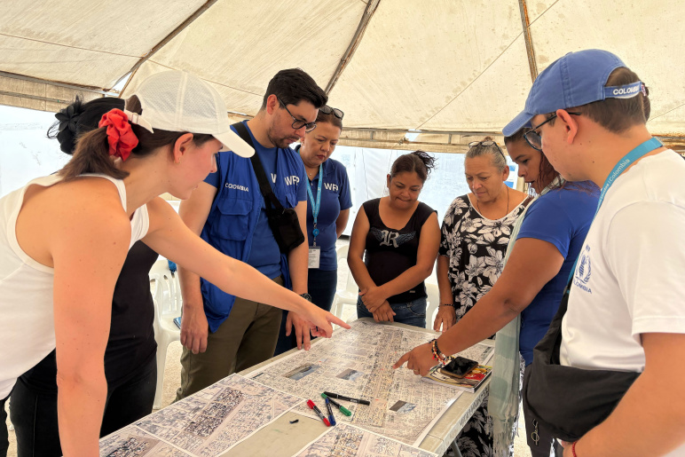 A group of people in a tent stand around a large map that is flat on a table