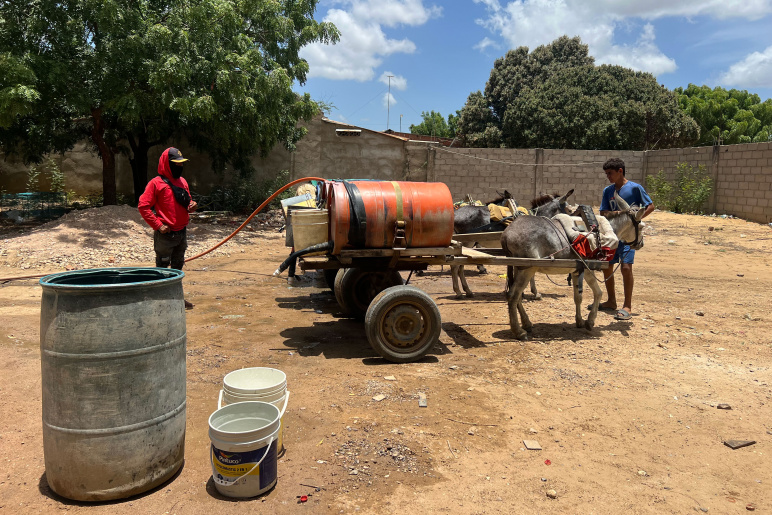 men standing with two donkeys attached to carts with large barrels on wheels. Some smaller barrels are seen in bottom left of image