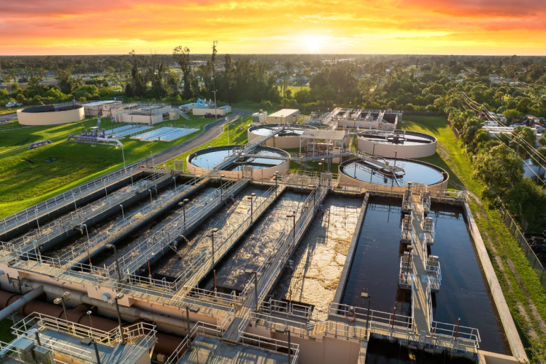 Water treatment facility with multiple tanks and filtration units shown from an aerial shot above with a setting sun in the background