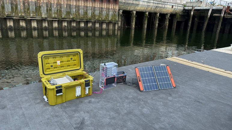 A portable desalination device in a yellow case next to a solar panel sitting on a dock