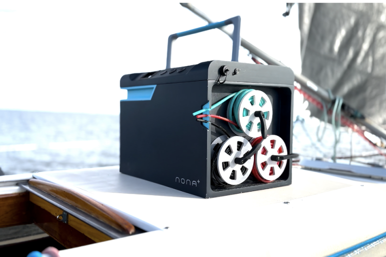 The portable desalination unit, a black box with three sets of wires coiled up on the side and a handle on the top, sitting on top of a sailboat on the ocean