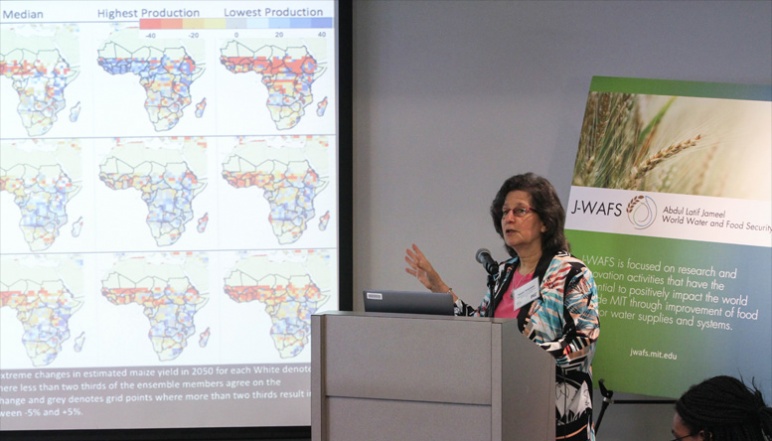Susan Solomon presenting at podium with maps of Africa on slide