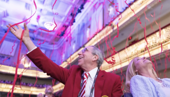 Older man and woman look up delightedly at red streamers falling from the ceiling.