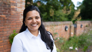 Mrinalini Penumaka outside against a brick building with shrubs in the background