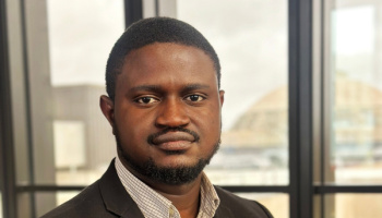 headshot of adeposi adeogun in a suit in front of a window