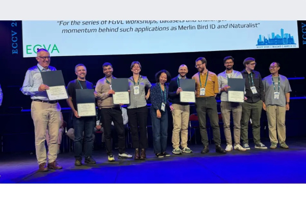 J-WAFS PI Sara and team standing on stage, holding PAMI prize certificates, blue floor