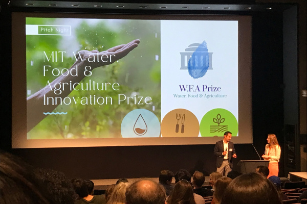 An auditorium full of people watch a presentation with two people at a podium and a slide that says inaugural MIT Water, Food & Agriculture Innovation Prize  