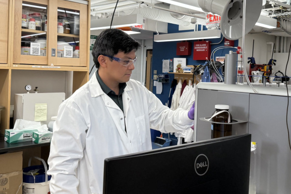 A person wearing a lab coat and goggles, looking at their work