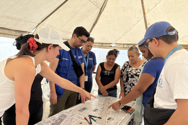 A group of people standing around a table, pointing to and discussing the maps on the table