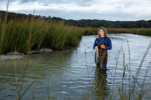 A woman standing in a coastal pond with tall grasses in the background. 