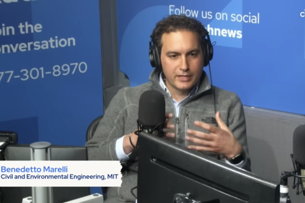 Benedetto Marelli wears a headset and sits in front of a large microphone in a radio show setting