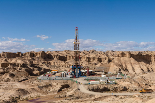 Drilling rig and industrial equipment in a rocky desert landscape.