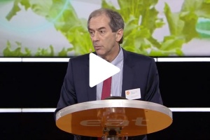 John Lienhard speaking at podium with play button on image