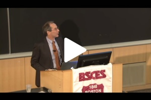 John Lienhard speaking at podium with play button on image