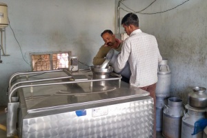 Two men pour large container of milk into machine