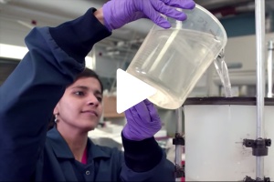 Researcher pouring water into filter with play button on image