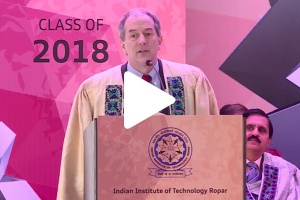John Lienhard speaking at podium with play button on image