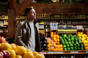 Man standing in grocery store with various colors of bell peppers behind him