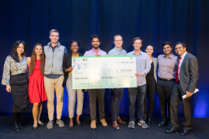 A group of ten young adults standing on a stage together holding a large check for $100,000
