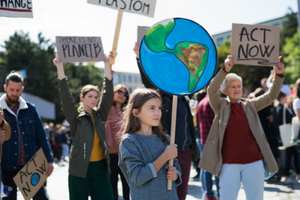 Crowd of people of a variety of age holding signs about climate change, including one that says "There is no planet B." In the front of the photo, a young girl is holding a sign with a globe on it.