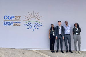 Four MIT students stand next to a sign reading COP27, Sharm El-Sheikh, Egypt, 2022