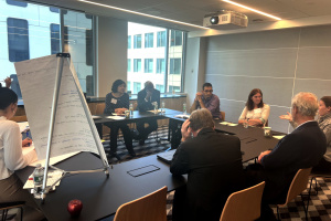 People sitting around a U-shaped conference room table with a flip chart on an easel