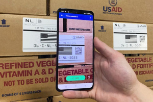 Closeup of a hand holding a smartphone, scanning a barcode on a cardboard package.