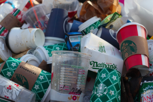 Single-use plastic cups and coffee cups in a trash pile