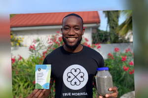 Kwami Williams holding a packet of moringa powder and some moringa seeds in a bottle
